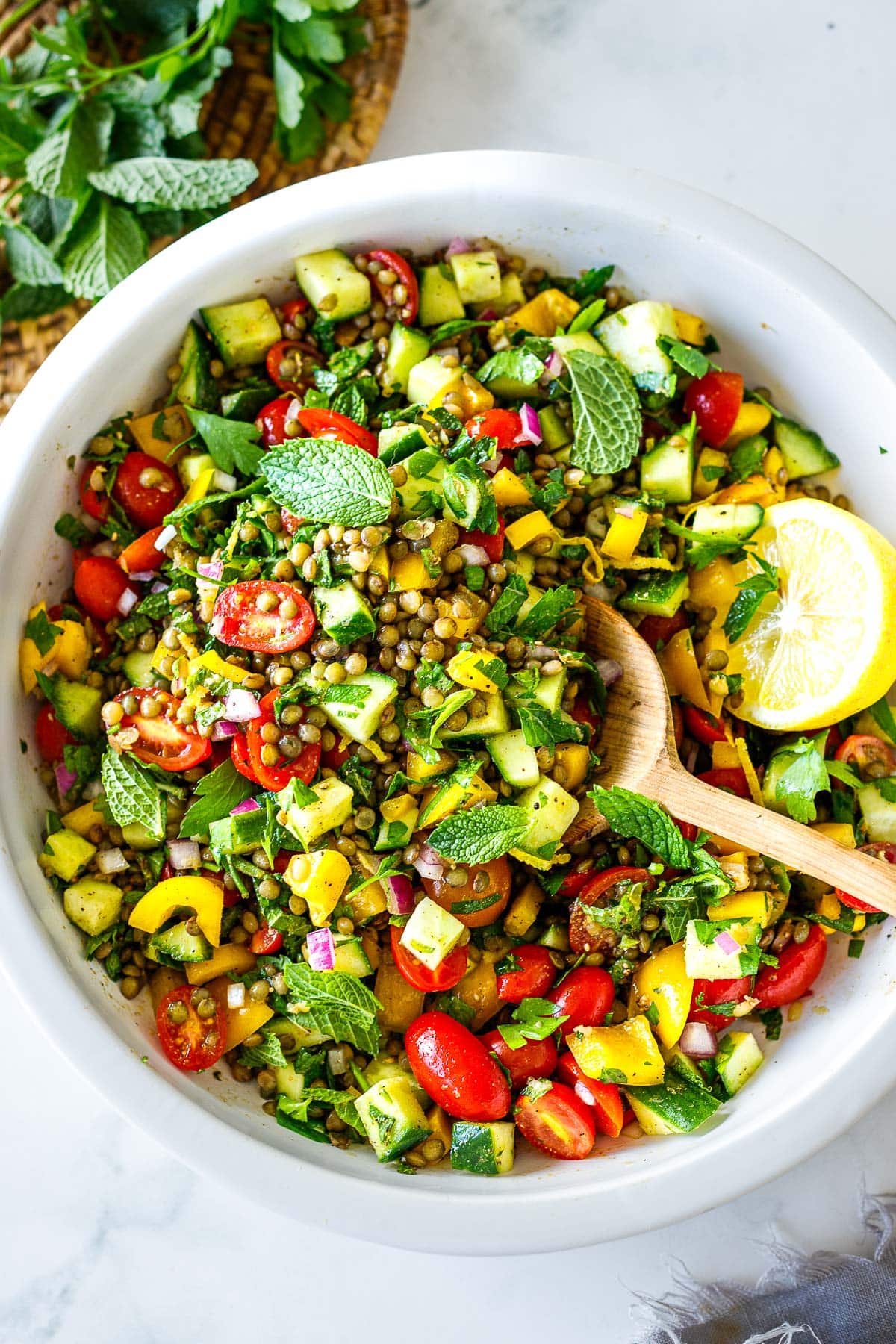 large salad bowl with mediterranean-inspired lentil salad garnished with mint and lemon, with wooden spoon. 