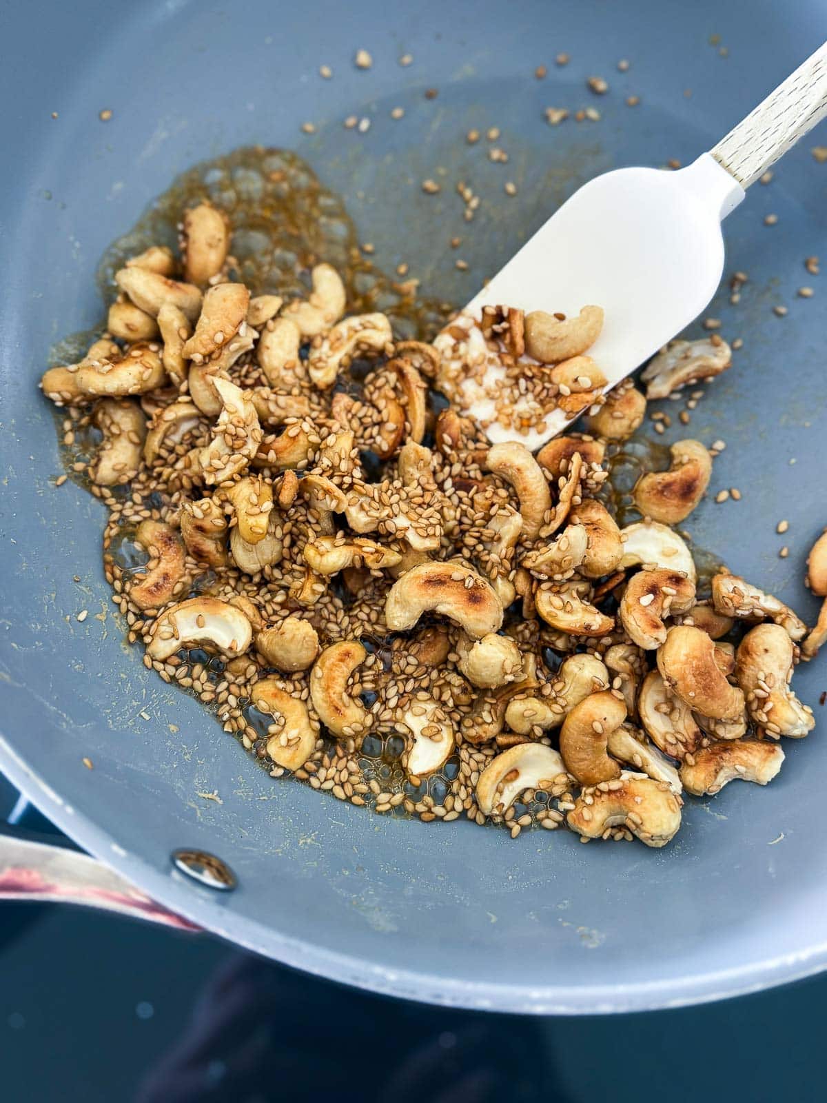 skillet with toasted cashews in sauce to make cashew brittle with white spatula. 