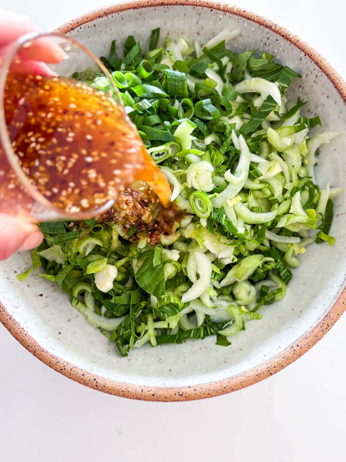 hand pouring sesame ginger dressing from jar onto bok choy salad. 