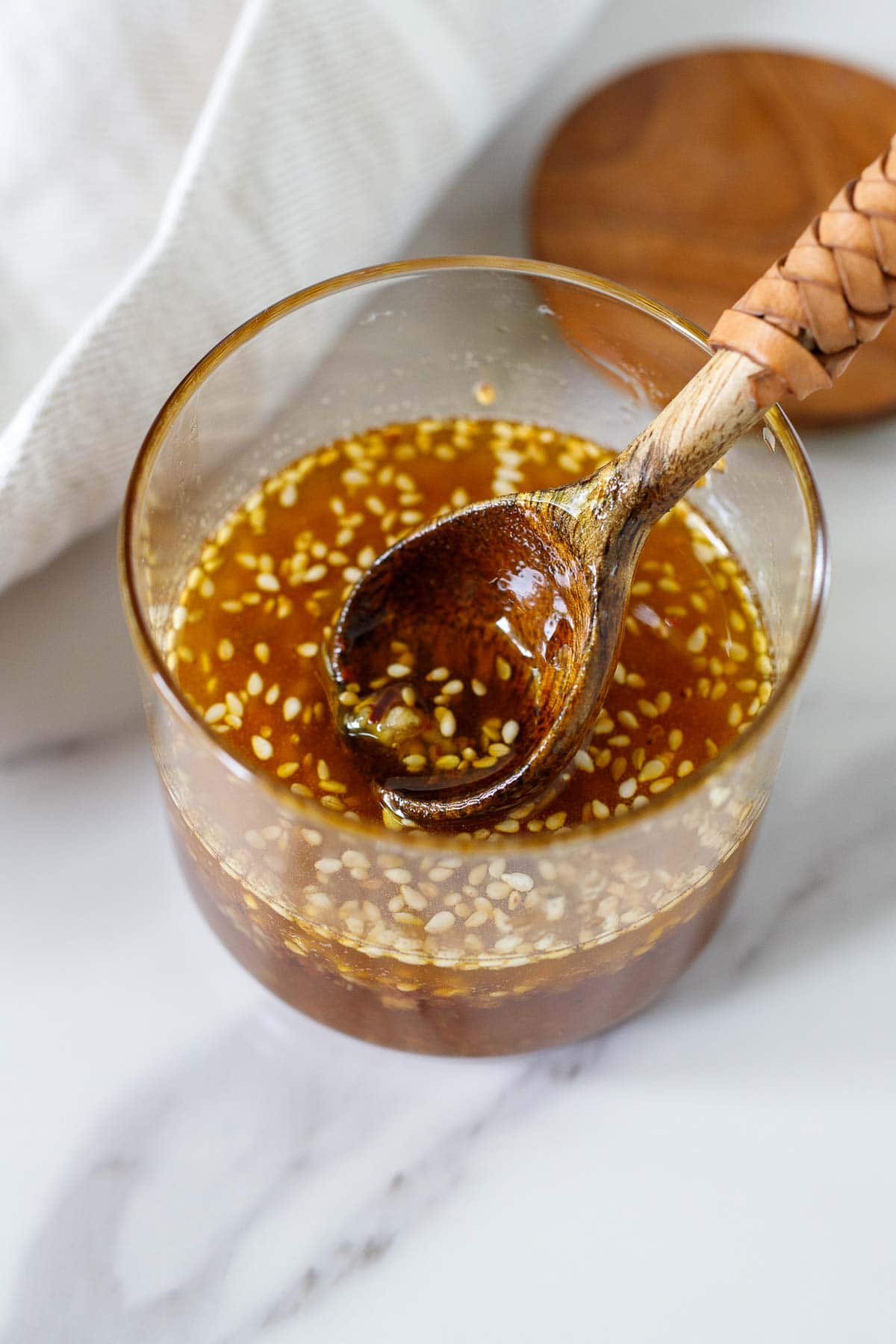 glass jar with sesame ginger dressing and small wood spoon with leather handle. 