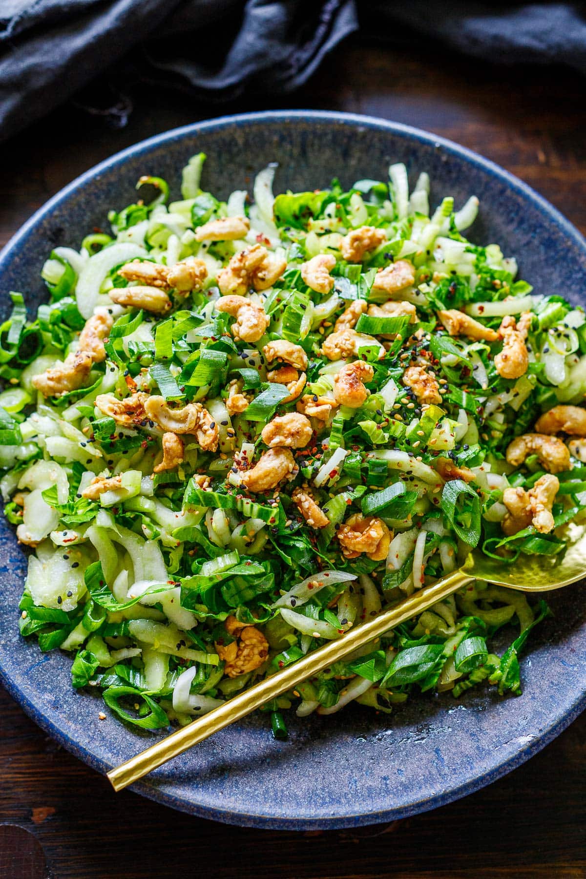 plate of bok choy salad with sesame ginger dressing and cashew brittle, with gold spoon.