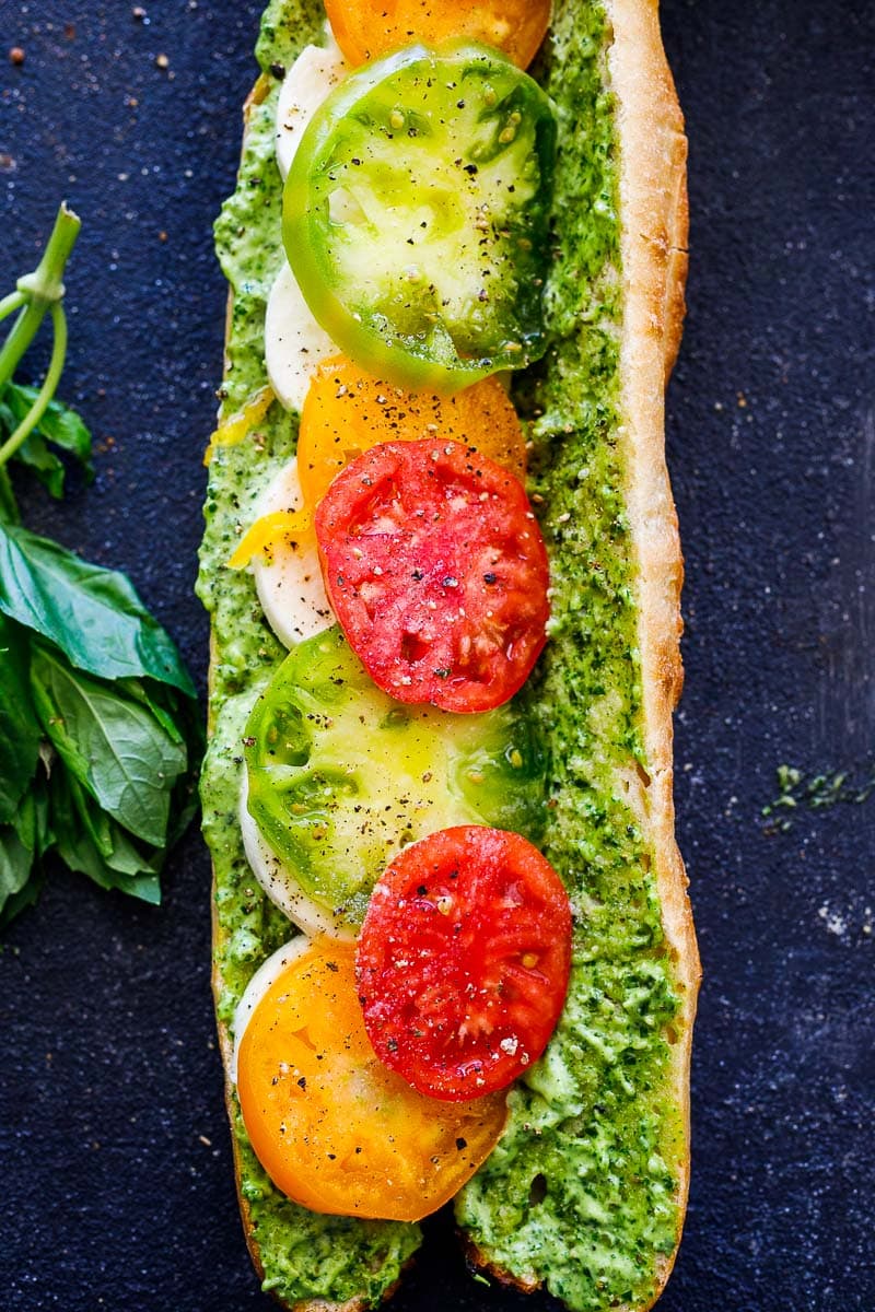 open caprese sandwich on baguette with pesto-mayo spread on each half, topped with mozzarella and juicy heirloom tomatoes. 