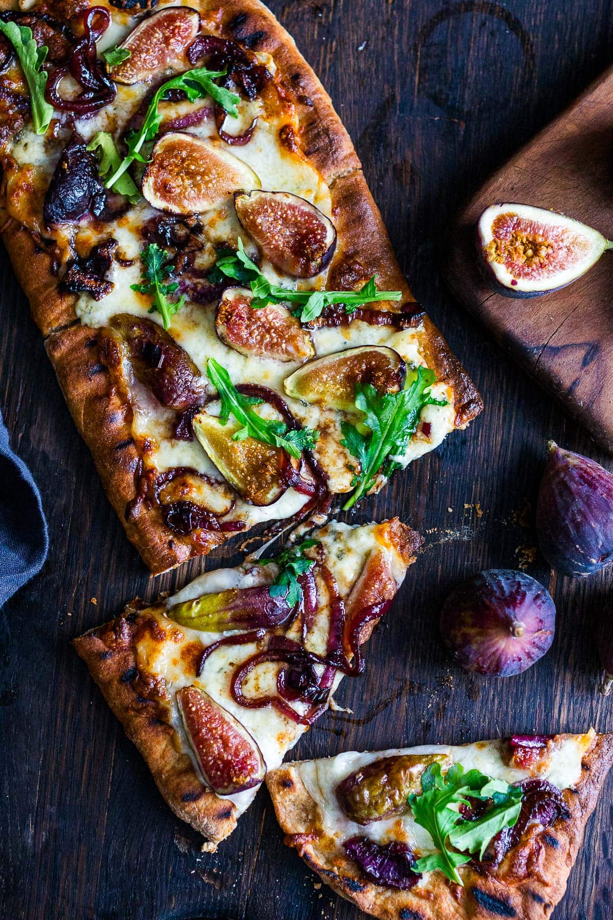 fig pizza garnished with arugula on wood board with two slices cut off. 