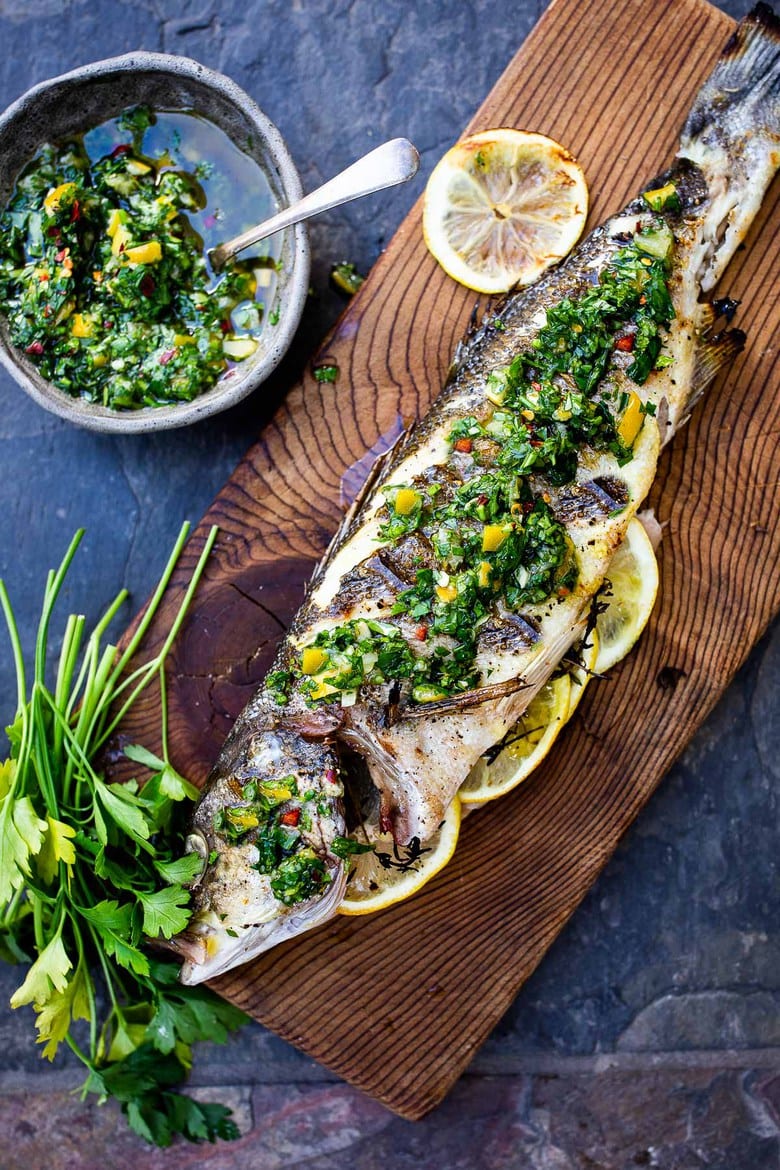 a whole grilled branzino on a wood plank with preserved lemon gremolata spread over top. 
