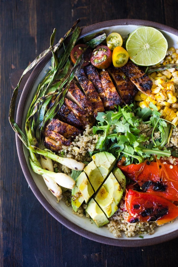 grilled chipotle chicken salad in bowl with quinoa, grilled corn, peppers, and scallions, cherry tomatoes, lime, avocado, and arugula. 