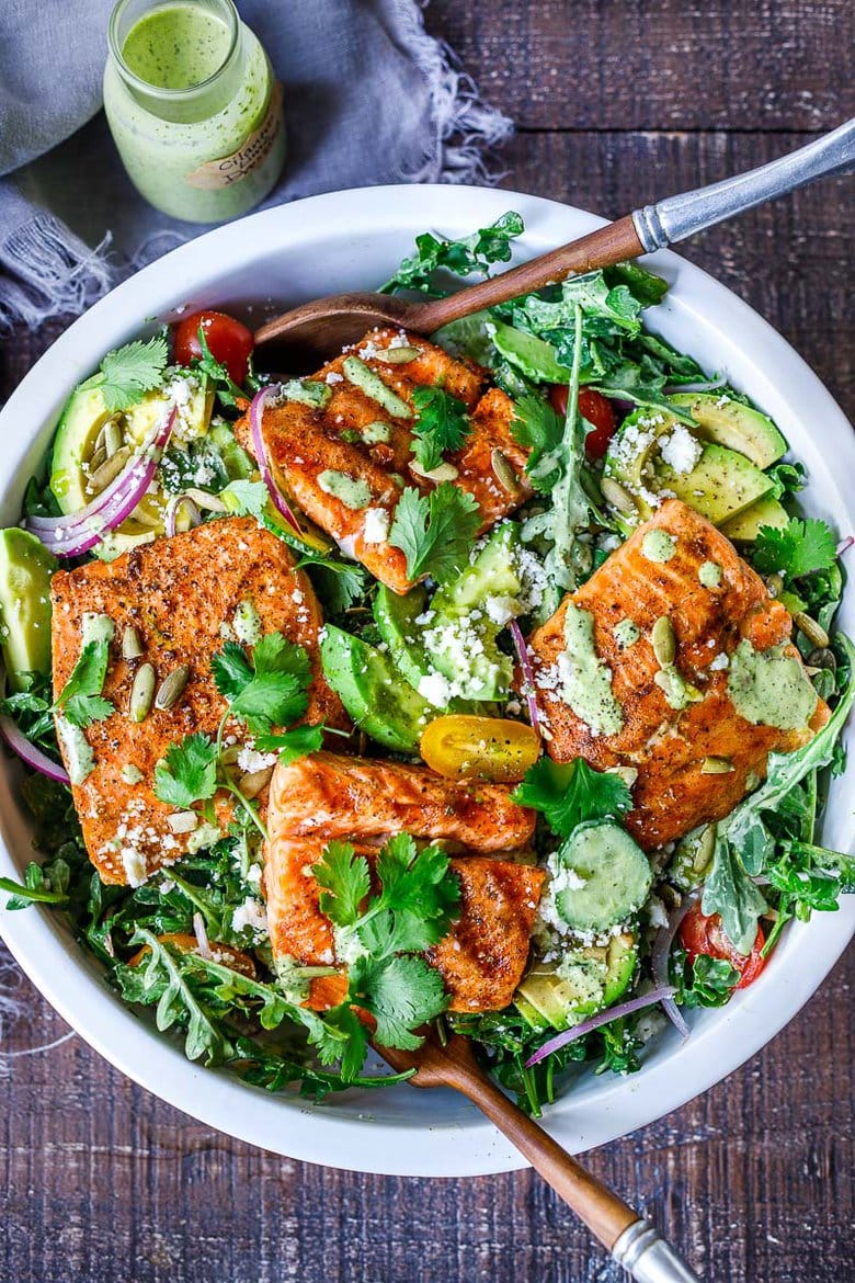 Salmon salad in a white bowl with avocado, pepitas, cilantro and a creamy cilantro dressing. 