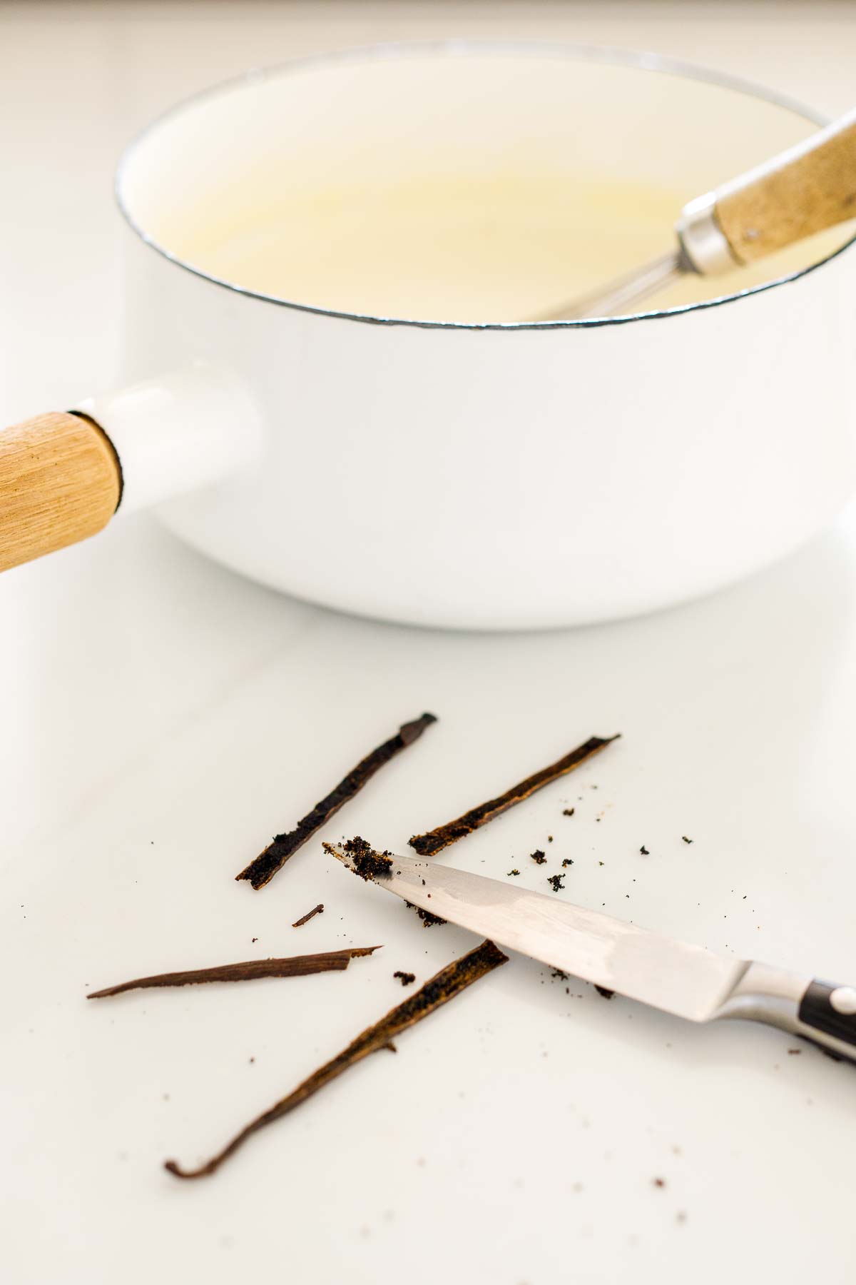 sharp knife scraping vanilla seeds from vanilla bean pods. 