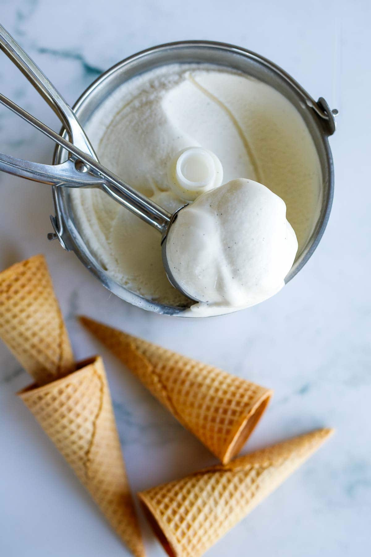 ice cream scoop with ice cream over ice cream churn surrounded by ice cream cones. 