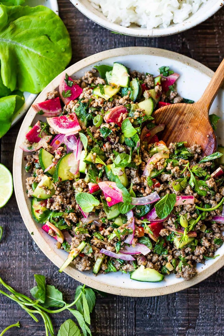 Thai larb salad in a a white bowl with cucumbers, radishes, mint and basil. 