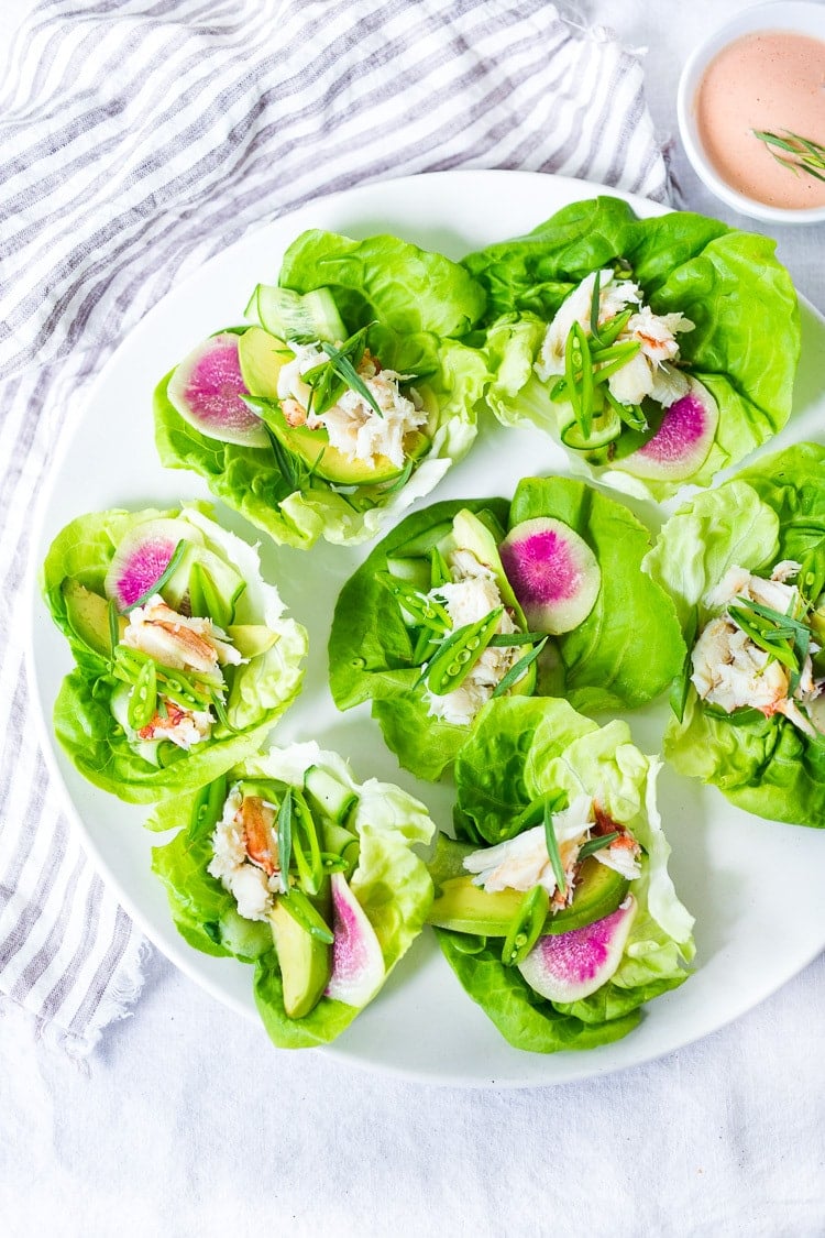 serving plate with mini crab louie lettuce wraps served with watermelon radish slices, avocado slices, and snap peas. 