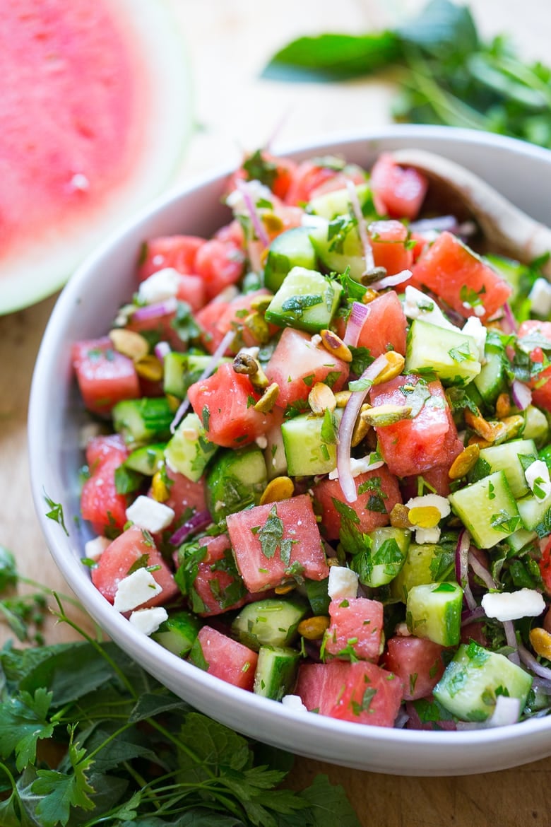 Moroccan watermelon salad with cucumber, red onion, crumbled feta, pistachios, and fresh herbs in bowl. 
