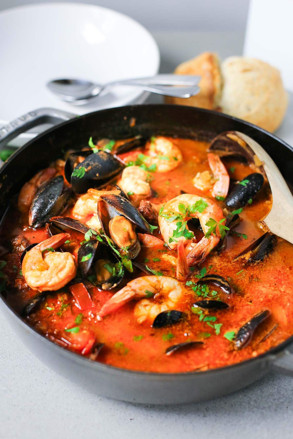 A braiser filled with seafood stew with a wood spoon for serving. 