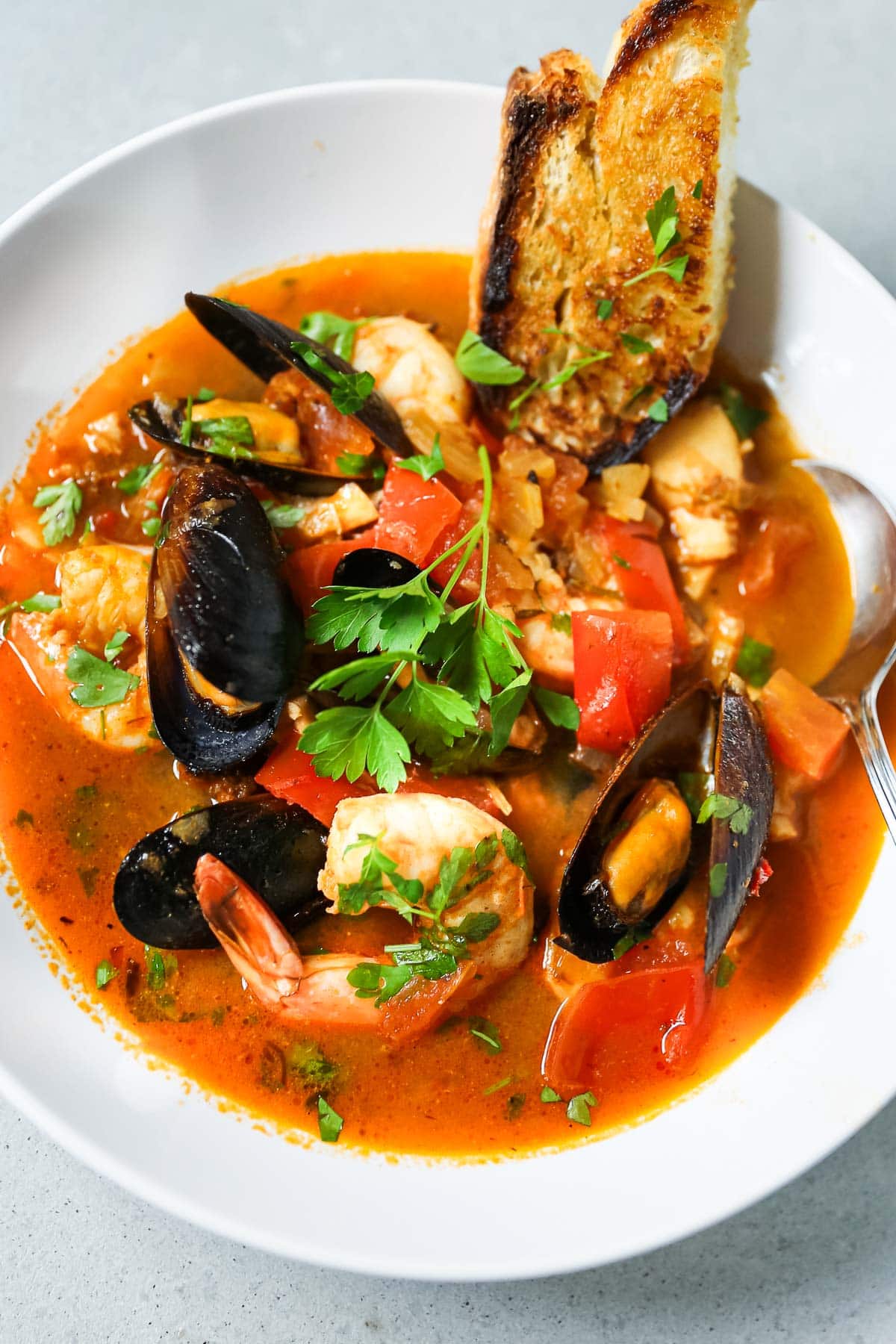 A white bowl full of seafood stew with mussels, shrimp, tomato broth. 