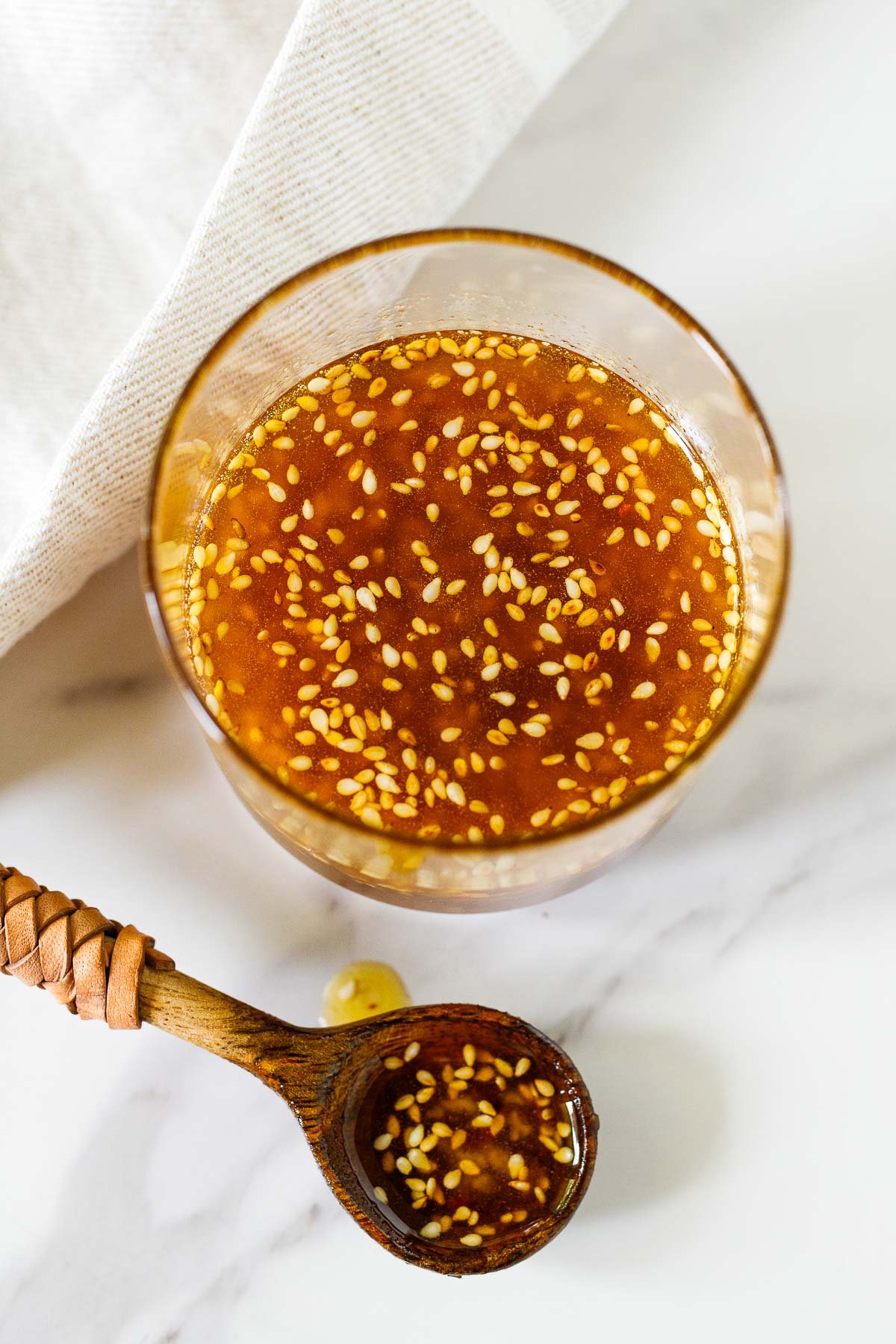 glass jar of sesame ginger dressing with small wood and leather spoon next to it, holding some of the dressing.