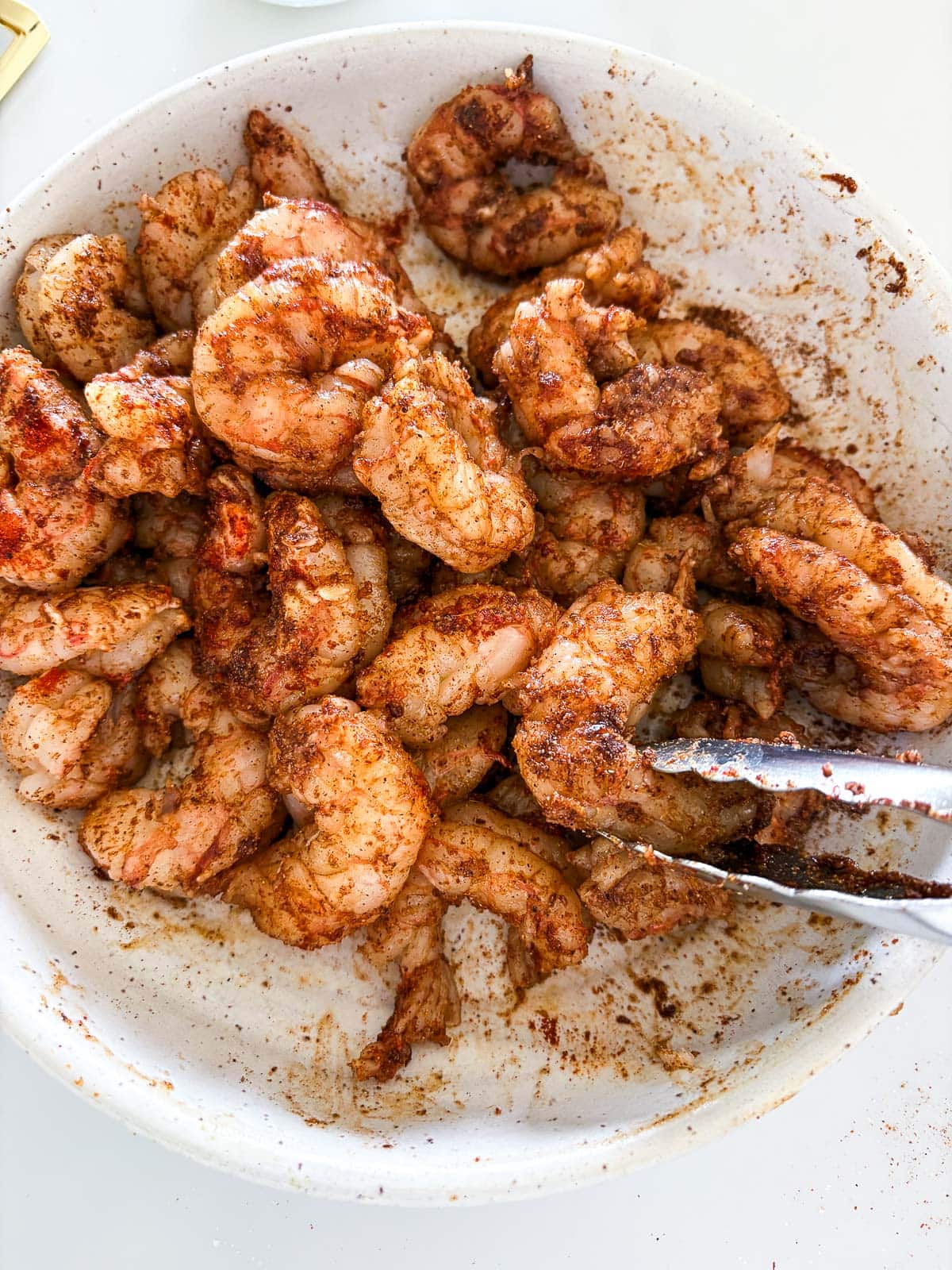 seasoned shrimp in a bowl with tongs. 
