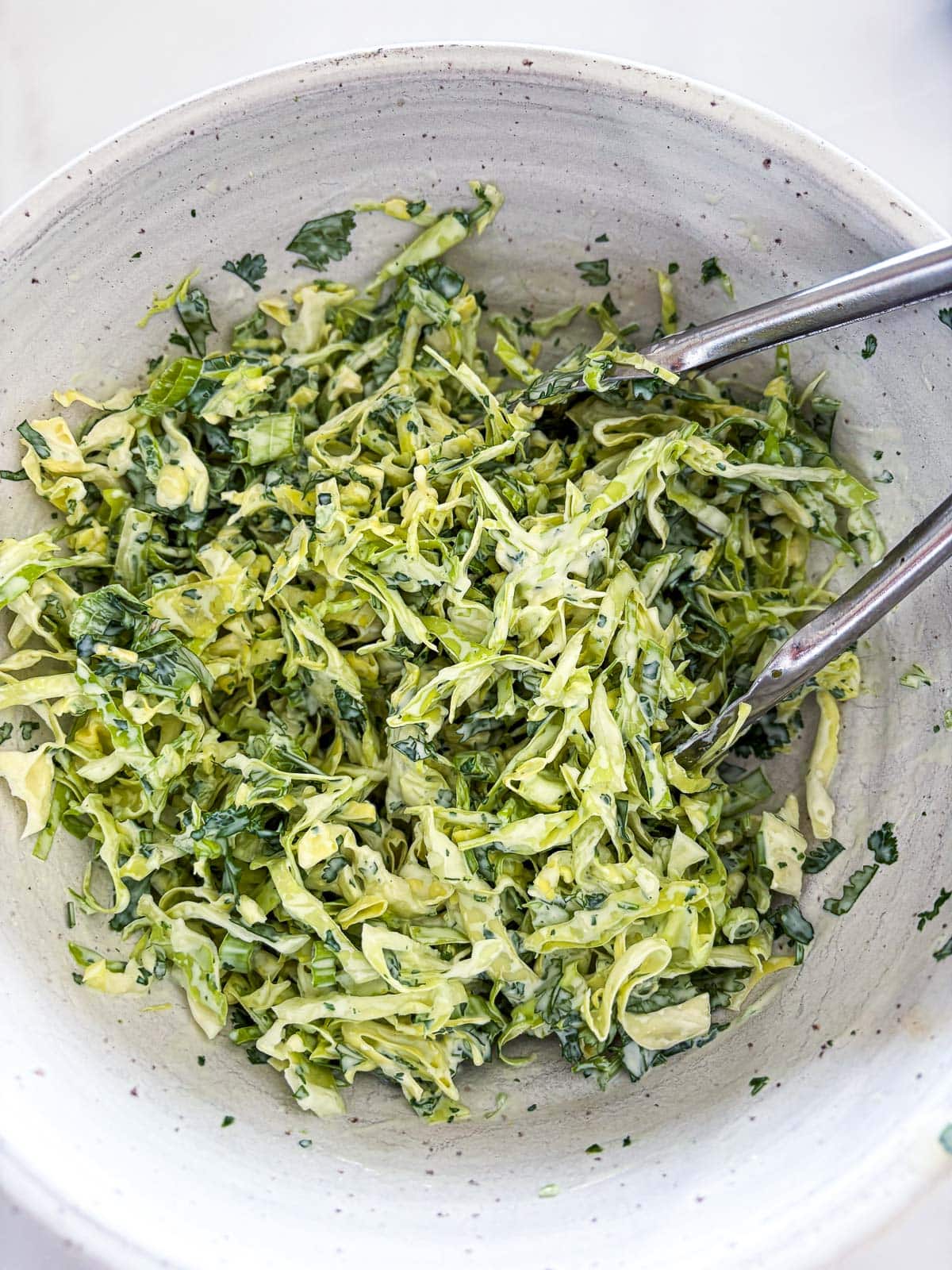 bowl of cilantro lime slaw with tongs. 