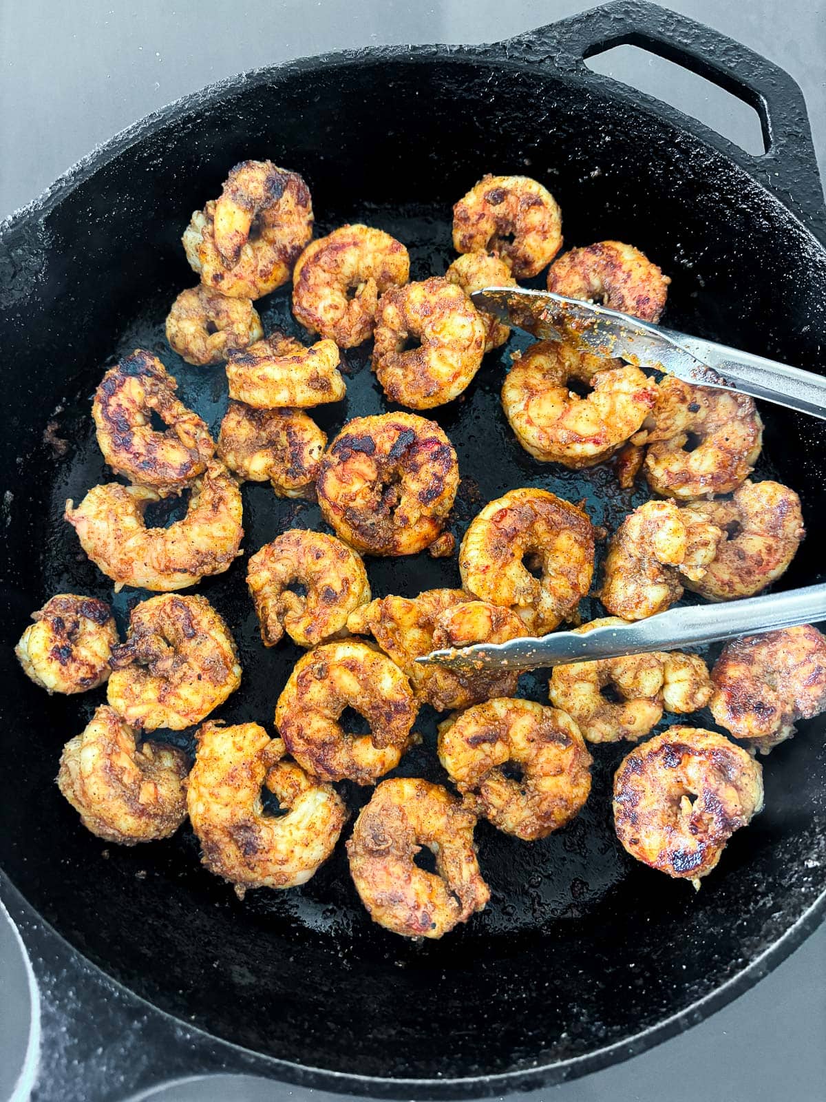 mexican shrimp searing in a cast iron skillet with tongs. 