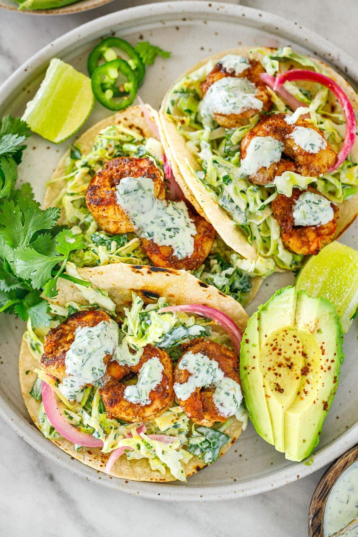 plate of shrimp tacos with cilantro lime slaw and cilantro lime crema served with avocado slices, limes, and cilantro. 