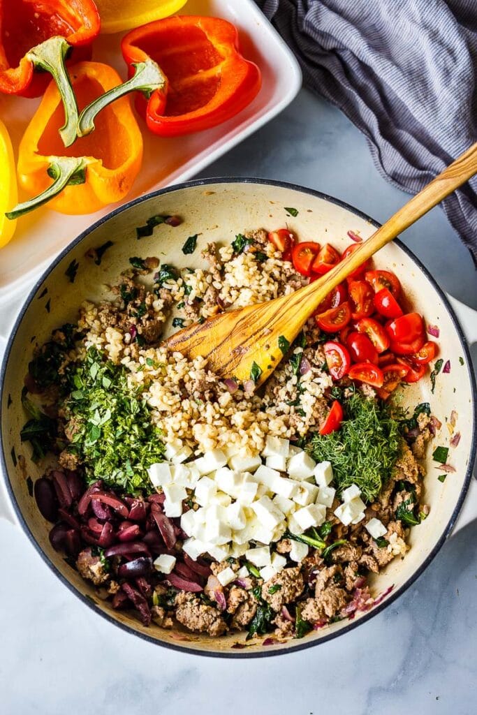 filling for mediterranean stuffed peppers in pan- wooden spoon mixing everything together.
