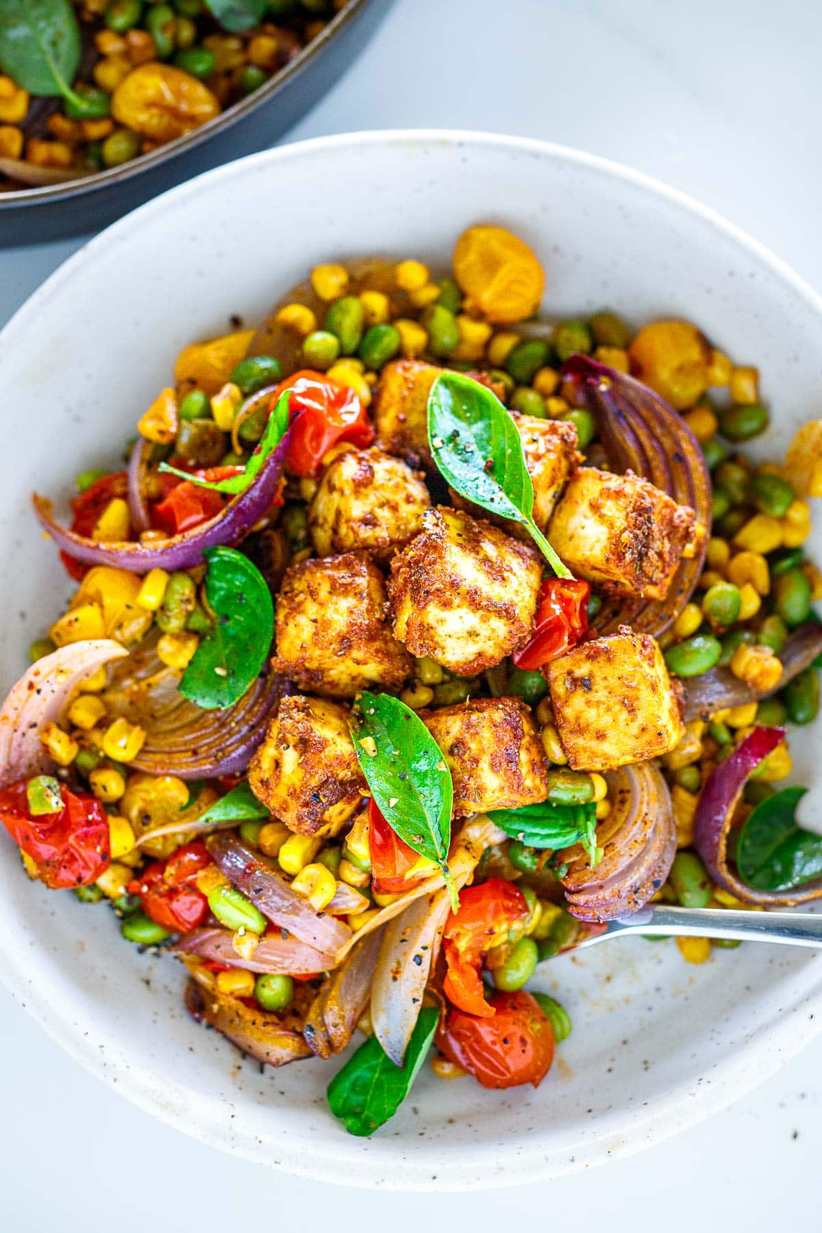 Crispy tofu served over baked succotash in a white bowl. 