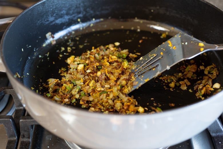 metal spatula stirring aromatics and curry paste in pan. 