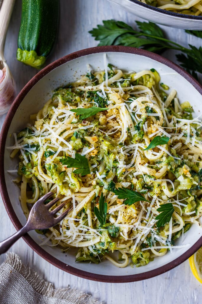 zucchini pasta sauce in bowl tossed with linguini and grated cheese and fresh parsley, with fork. 